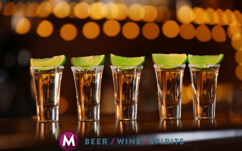 Five tequila shots with lime wedges lined up on a bar counter, highlighting June spirits specials at Mulberry Max